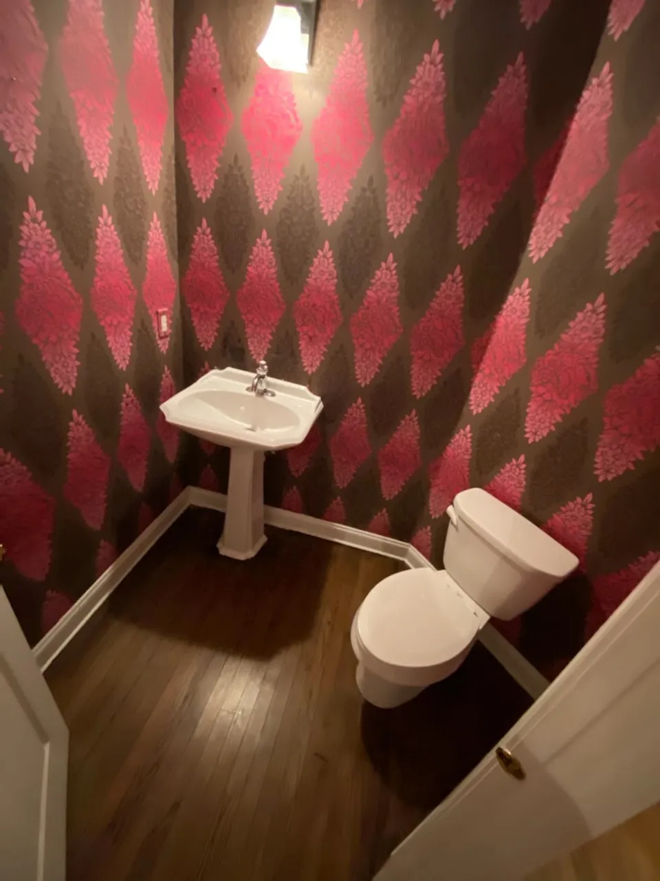 Compact powder room with pink wallpaper and a white sink