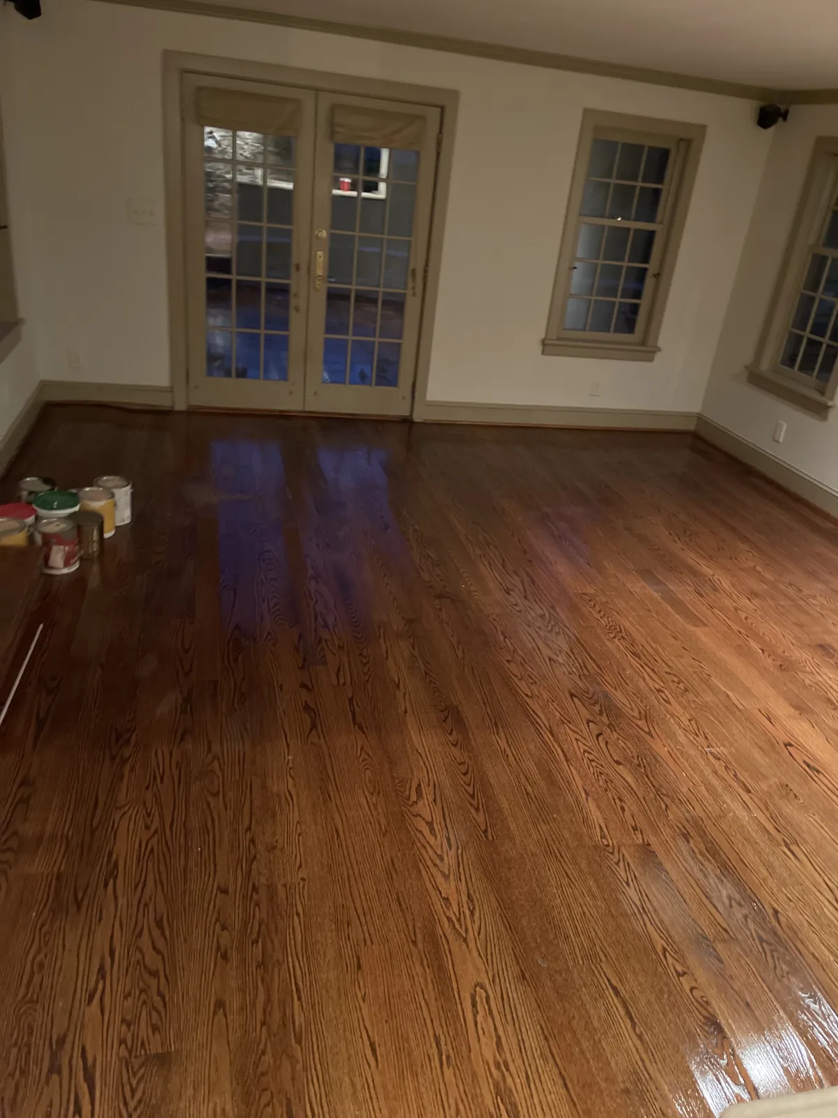 Empty room with polished hardwood flooring and paint cans