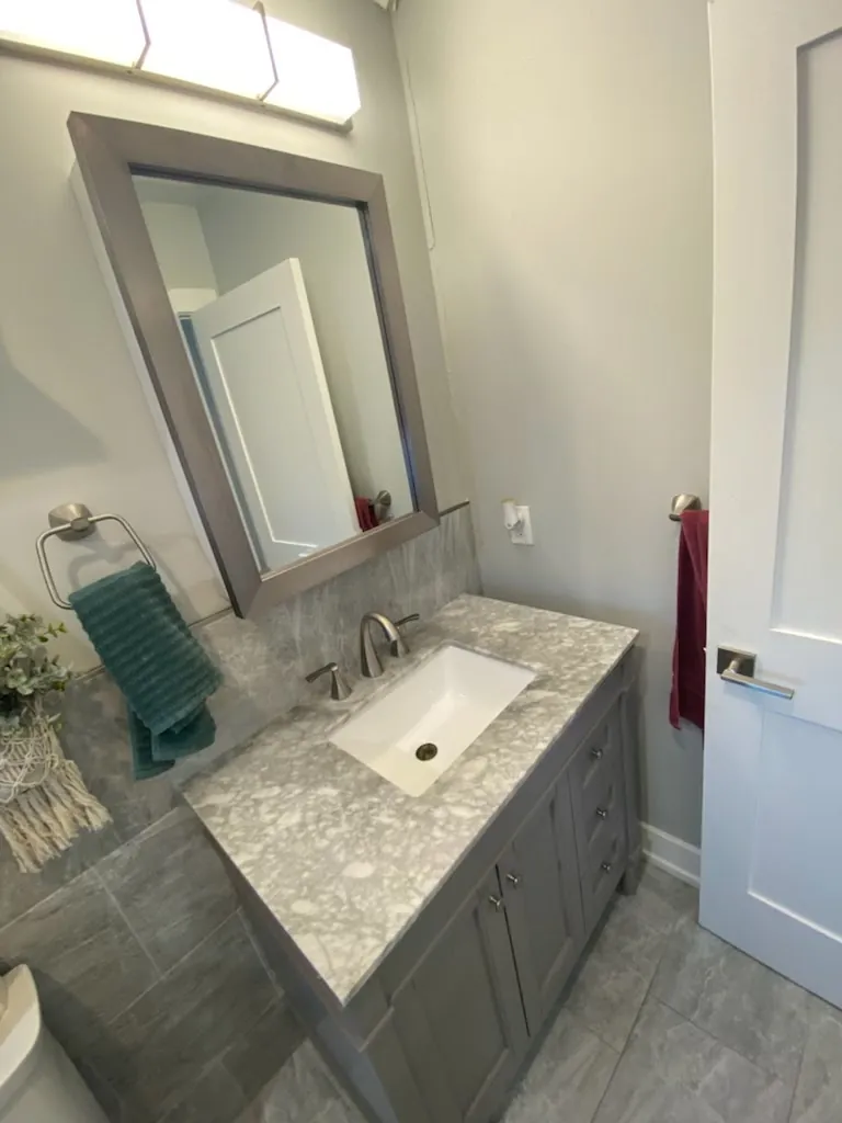 Modern bathroom with a gray vanity, round mirror, and glass shower