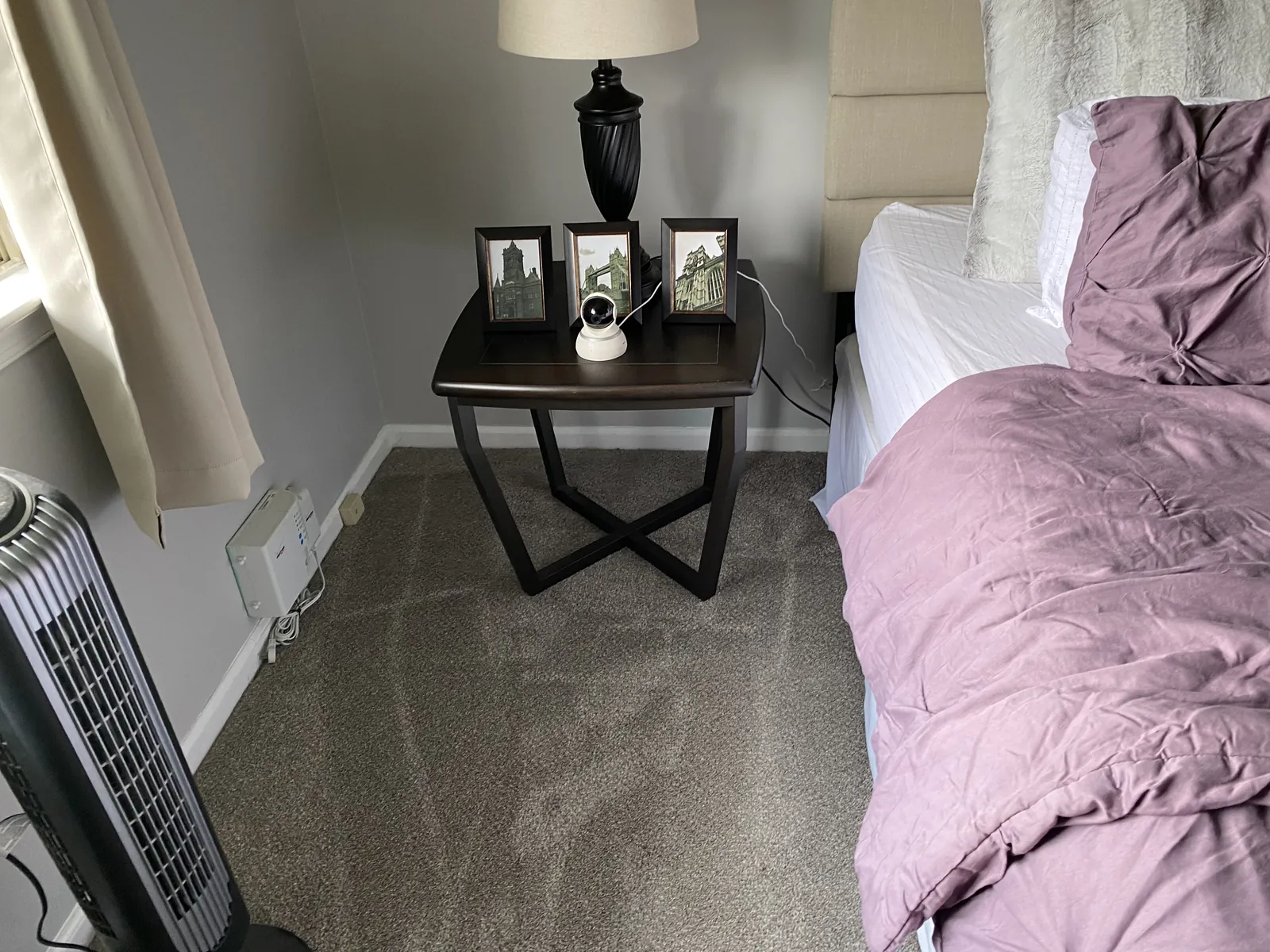 Bedroom with a made bed, side table, and light carpet